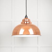 The Arcus Spun Pendant Light in Copper and Glossy White Shown Lit up on a White Panelled Background