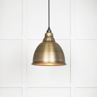 The Aura Dome Pendant Light in Aged Brass Shown Lit up on a White Panelled Background