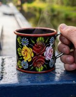 The Black Buckby Narrowboat Style Hand Painted Mug with a Hot Drink inside with Hand in Shot for Scale - Digital Illustration