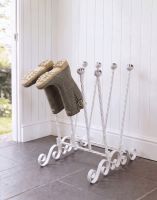 The Evesall Cream 4 Pair Ornate Boot Rack Positioned on a Stone Tile Floor in a Sunny Garden Porch - Digital Illustration 