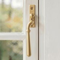 The Left Handed 16mm Modern Satin Brass Espagnolette Window Handle Mounted on a Classic White Coloured Window Frame in a Country Home - Digital Illustration