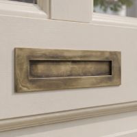 The Modern 10 Inch Front Door Letter Plate with Contemporary Minimalist Flap in Aged Brass on a Cream Coloured Front Door to a Regency Style Door - Digital Illustration
