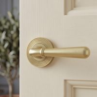 The Modern Satin Brass "Neville" Beehive Door Handle on Rose Set Fitted to a Cream Door in a Modern Home Setting - Digital Illustration