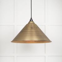 The Nidus Pendant Light in Aged Brass on a White Panelled Background with Light on