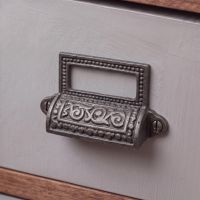 The Ornate Iron Drawer Pull With Label Holder Shown Close up on a Light Purple Set of Drawers - Digital Illustration The Ornate Iron Drawer Pull With Label Holder Shown Close up on a Light Purple Set of Drawers - Digital Illustration