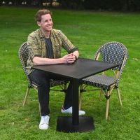 The Parisienne Bistro 2 Seater Outdoor Dining Set in Black and White Shown on. a Garden lawn with a Man Sat at the Table