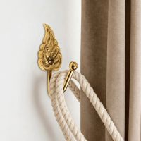 The Polished Brass Curtain Hook in a Leaf Design Fitted on a White Wall in a Modern Interior Home Next to a Brown Curtain - Digital Illustration The Polished Brass Curtain Hook in a Leaf Design Fitted on a White Wall in a Modern Interior Home Next to a Brown Curtain - Digital Illustration