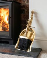 The Polished Brass Fireplace Pan and Brush Set next to a Traditional White Fireplace with a Log Burner Stove - Digital Illustration
