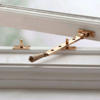 The Polished Bronze Georgian Reeded Casement Window Stay Fitted on a White Window Frame - Digital Illustration The Polished Bronze Georgian Reeded Casement Window Stay Fitted on a White Window Frame - Digital Illustration