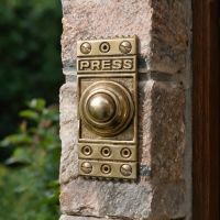 The Retro "Push" Polished Brass Door Bell Push on a Stone Brick Wall next to a Wooden Front Door - Digital Illustration