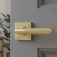 The Satin Brass "Royale" Square Unsprung Door Handle on Rose Set Shown Close up on a Modern Grey Door - Digital Illustration