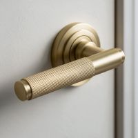 The Satin Brass "Royale" Unsprung Art-Deco Door Handle on Rose Set Shown Fitted on a Grey Door in a Modern Home - Digital Illustration
