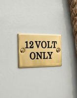 The Solid Brass Plaque With Black Lettering Label that Reads "12 volt only" Shown Close up on a Narrow Boat - Digital Illustration