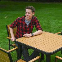 The Strata Slatted 4-Seater Outdoor Dining Set in Black With a Smiling Man Leaning on the Table