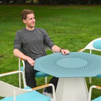 The Vortex Rotating Octagonal 4-Seater Outdoor Dining Set with a Man Sat at the Table on a Garden Lawn