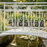 The Westminster Victorian Ornate Wrought Iron Garden Bridge in a White Finish Shown in a Sunny Private Garden over a Small Stream Focussing on the Central Scroll Work - Digital Illustration The Westminster Victorian Ornate Wrought Iron Garden Bridge in a White Finish Shown in a Sunny Private Garden over a Small Stream Focussing on the Central Scroll Work - Digital Illustration