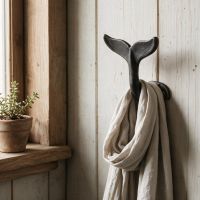 The Whale Tail Cast Iron Coat & Hat Hook Shown next to a Window in a Wooden porch - Digital Illustration 