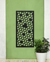 Black "Honeycomb Pattern Wall Art" mounted on a green wall next to a potted house plant