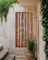 Rust Finish "Bamboo Garden Wall Art" on a cream brick wall next to stairs and plants Rust Finish "Bamboo Garden Wall Art" on a cream brick wall next to stairs and plants
