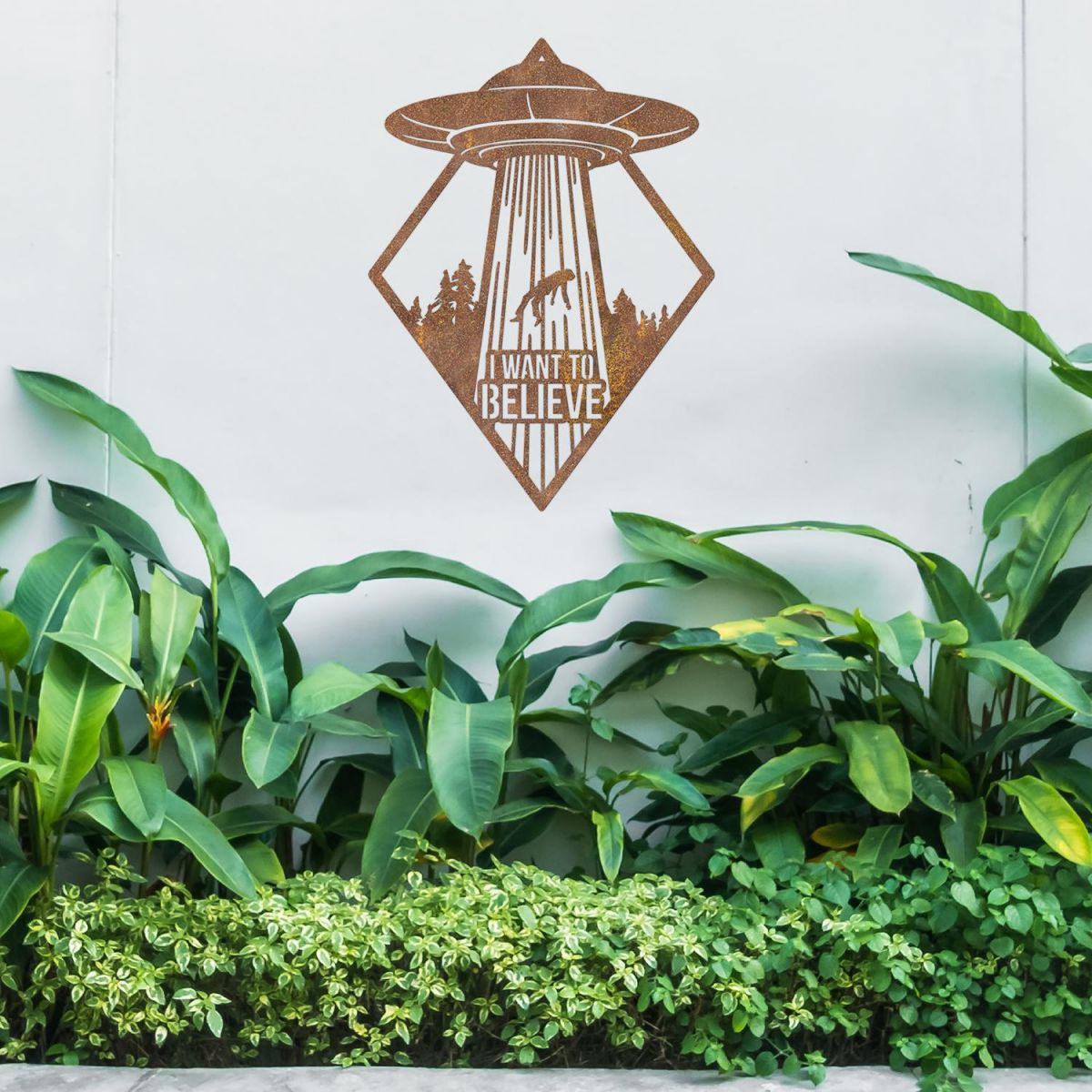 "I Want to Believe" Alien Wall Art Above a Bush Outdoors