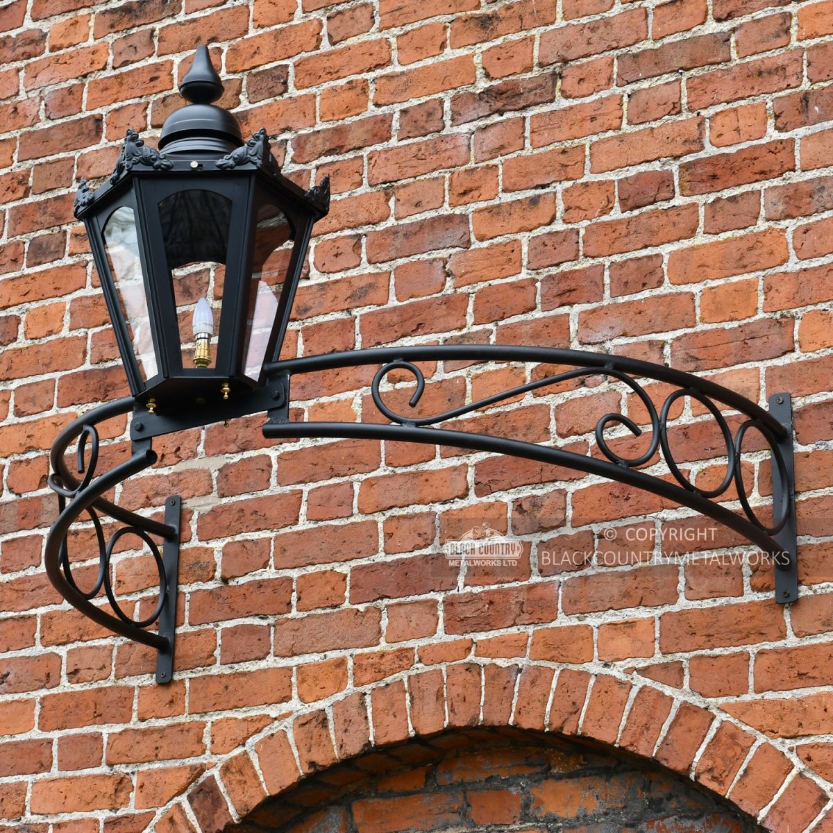 Black bow bracket with black lantern above archway on brick wall