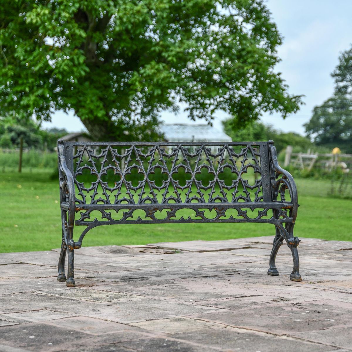Aged Black "Quatrefoil" Victorian Cast Iron Two Seat Bench in Use in the Garden