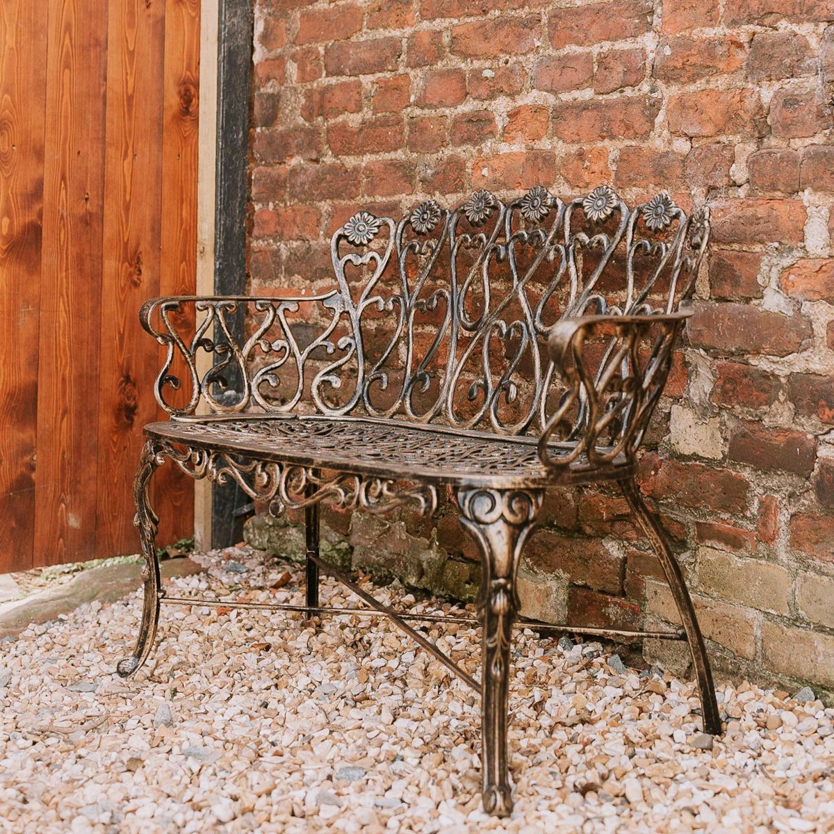 "Chorley" Brushed Gold Bench Next to a Brick Wall in the Garden