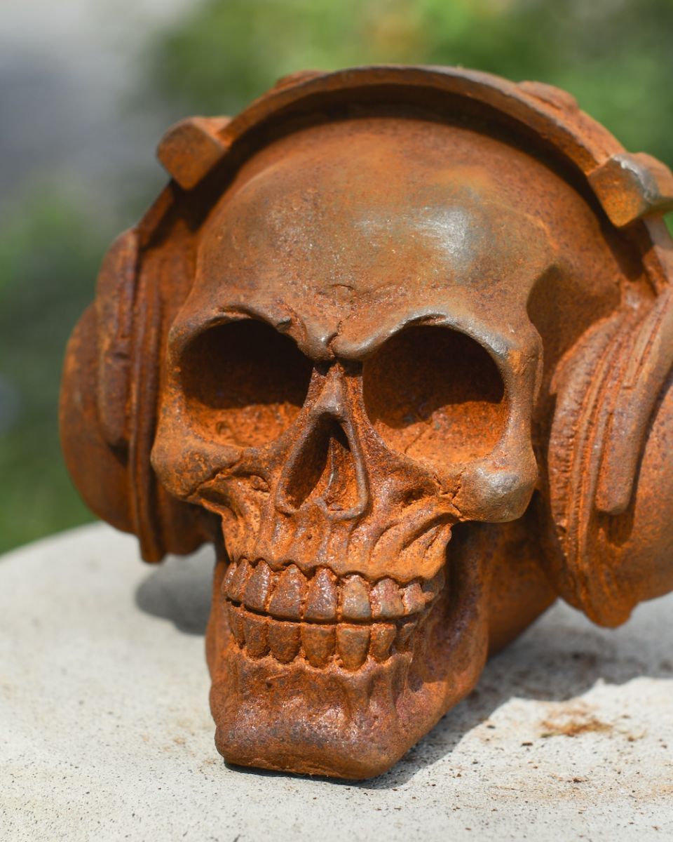 Detailed close up of rusted cast iron skull wearing headphones garden ornament