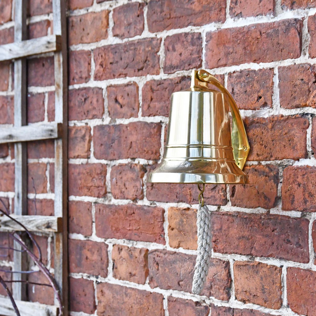 Polished Brass Bell with Rope Lanyard on Brick Wall
