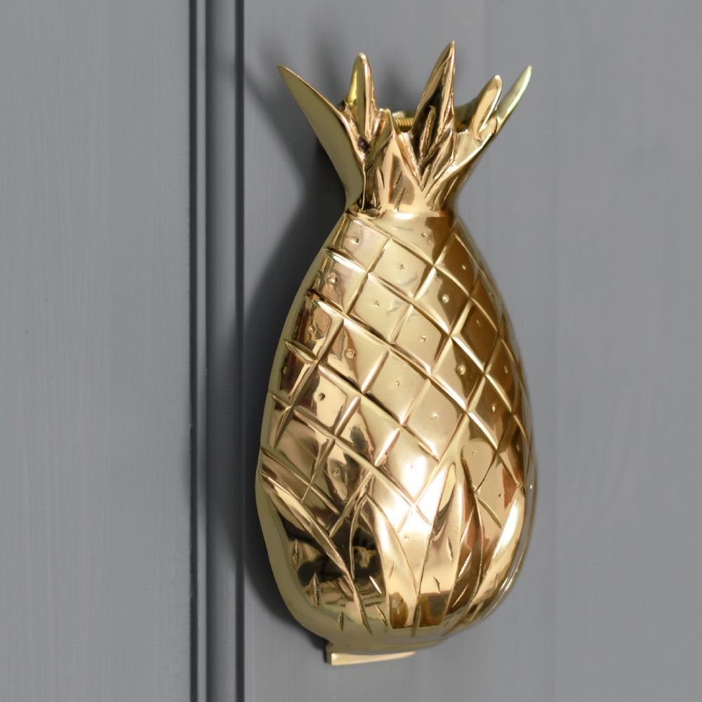 Polished brass pineapple door knocker on a grey door