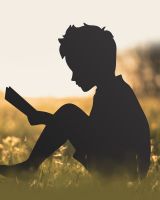 Boy With Book Silhouette sitting on grass in the sunset