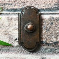 Arched burnished copper door bell on brick wall
