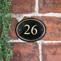 Polished Brass & Black Oval House Number Sign With Vinyl Numbers on a Brick Wall