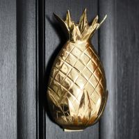 Polished brass pineapple door knocker on a black door