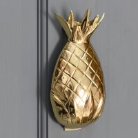 Polished brass pineapple door knocker on a grey door