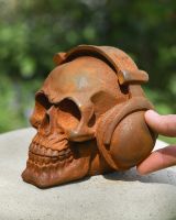 Scale picture of rusted cast iron garden ornament of skull wearing headphones