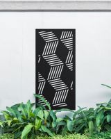 Black "Geometric Cube Wall Art" mounted on a white garden wall surrounded by garden plants