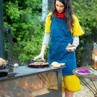 Woman Cooking Using Large Outdoor Wood Burner 