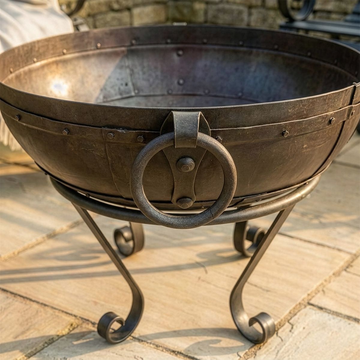 Digital Illustration of the 60cm Version of the Iron Kadai Bowl Fully Lit in Front of Rustic Garden Furniture Handle Close Up