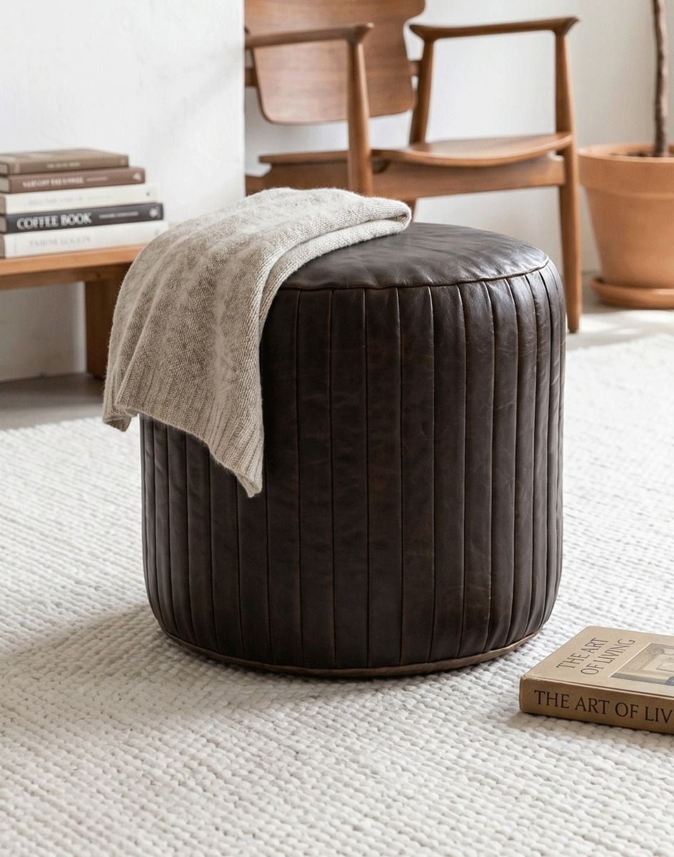 "The Coll" Brown Leather Round Pouffe in a Living Room with a Grey Blanket on top - Digital Illustration