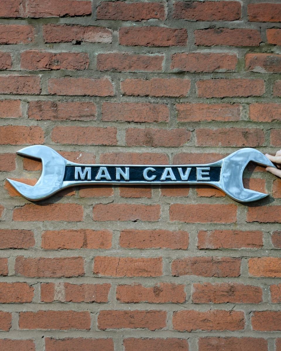 "Man Cave" Spanner Sign in Cast Aluminium Wall Art Mounted on a Brick Wall with Hand in Shot for Scale