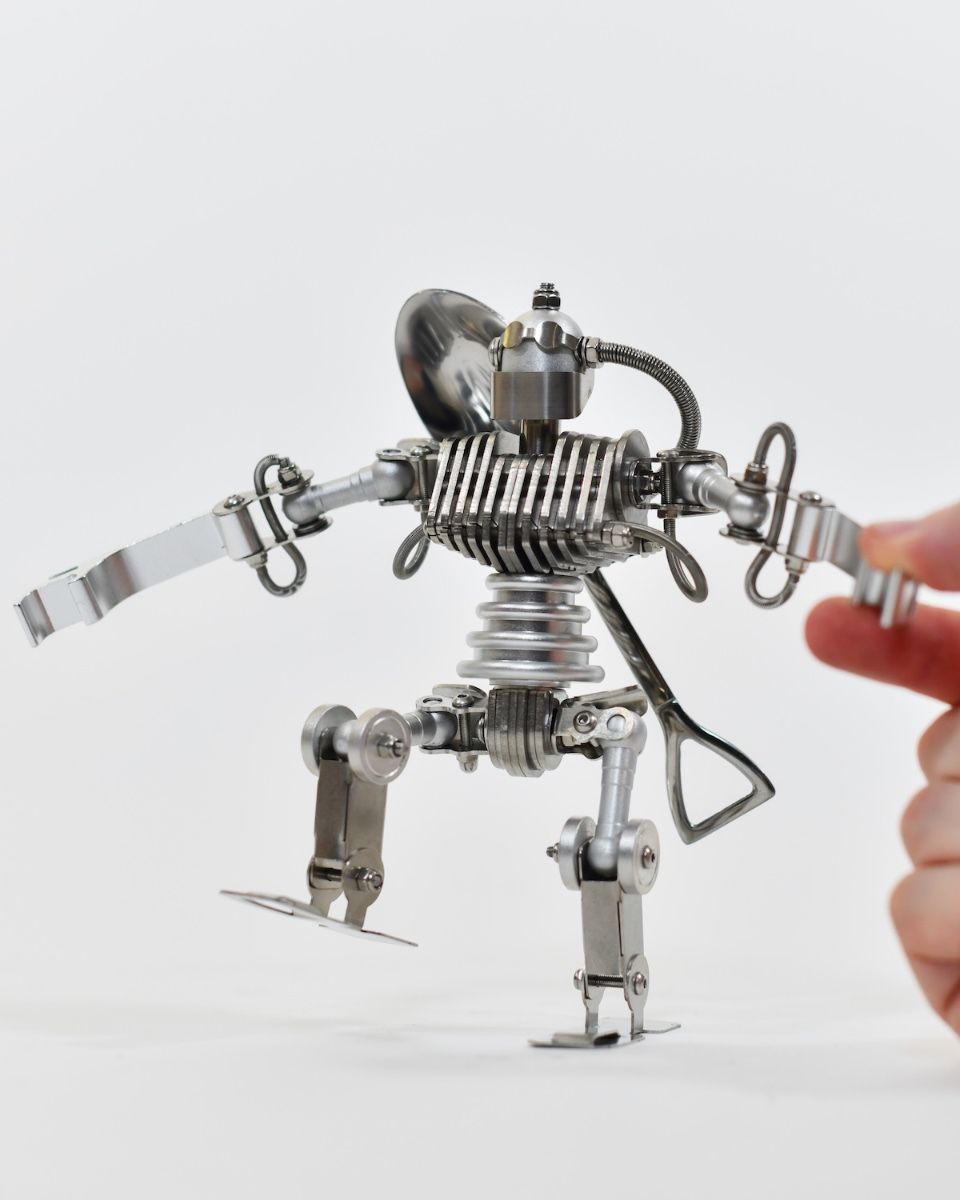 ‘Stainless Sentinel’ Upcycled Stainless Steel Robot walking forward with hand to reference scale