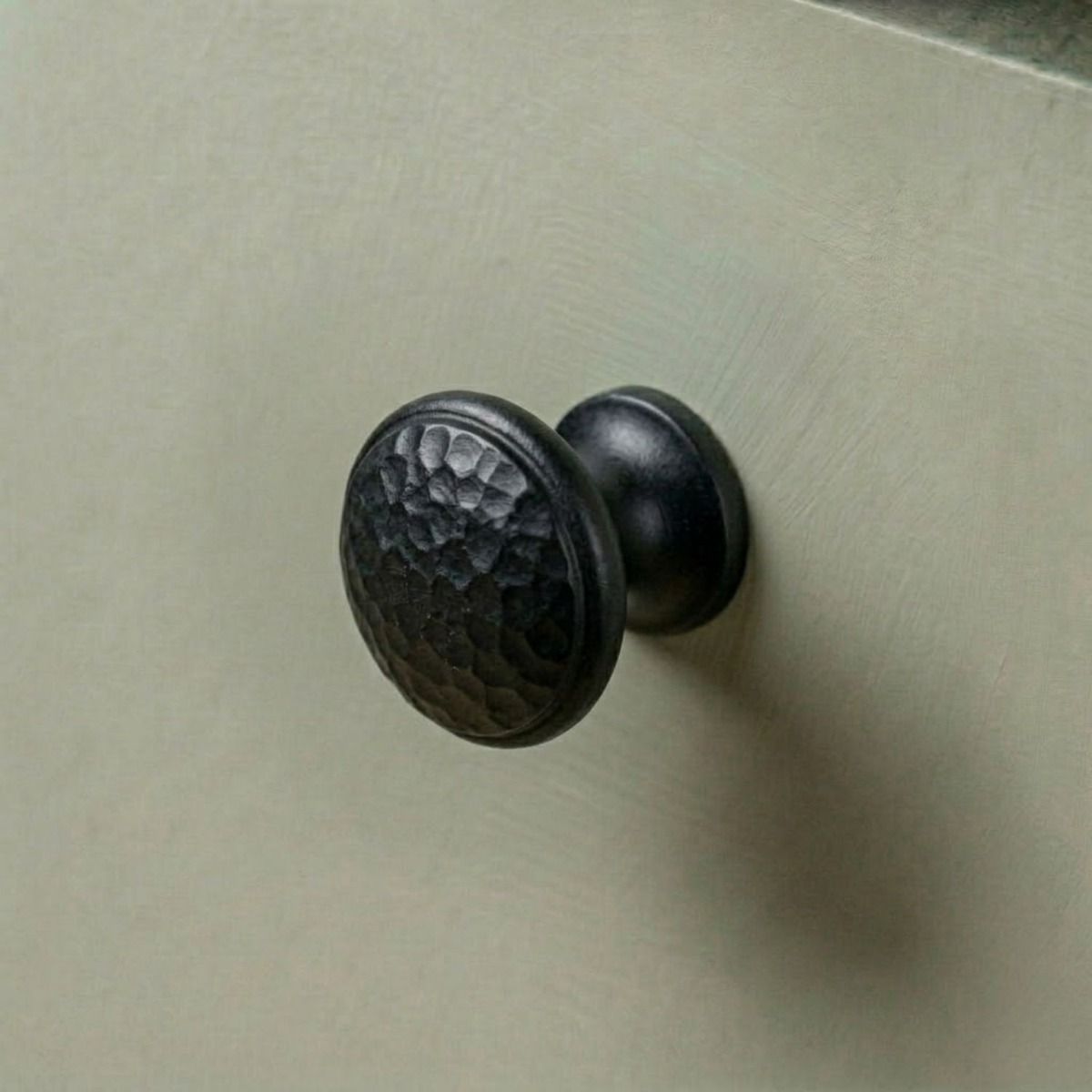A 30mm Black Hammered Iron Cabinet Knob Mounted on a Light Green Kitchen Cupboard - Digital Illustration 