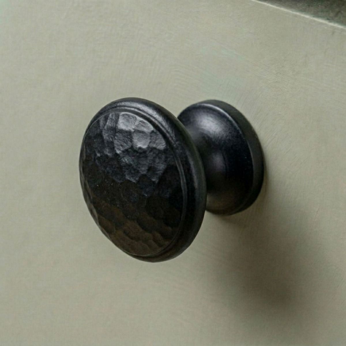 A 40mm Black Hammered Iron Cabinet Knob Placed on a Green Kitchen Cupboard - Digital Illustration 