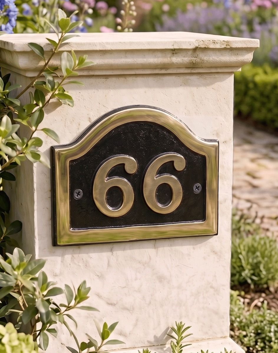 A Number 66 Arched House Number Sign in a Black and Brass Finish Mounted on a Driveway Entrance Wall - Digital Illustration 