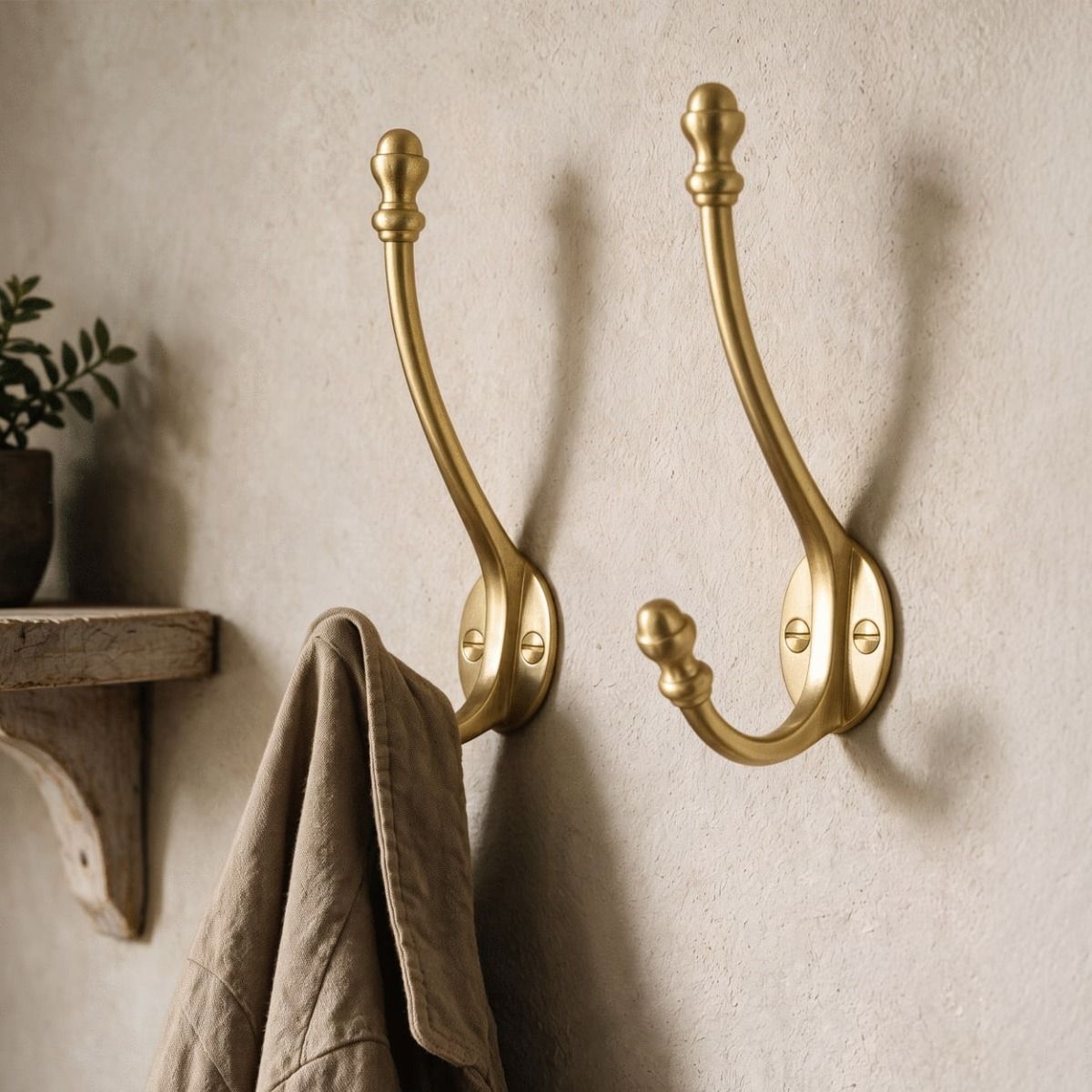 A Pair of 86mm Satin Brass Double Hat & Coat Hooks Positioned in a Hallway Next to a Wooden Shelf - Digital Illustration 