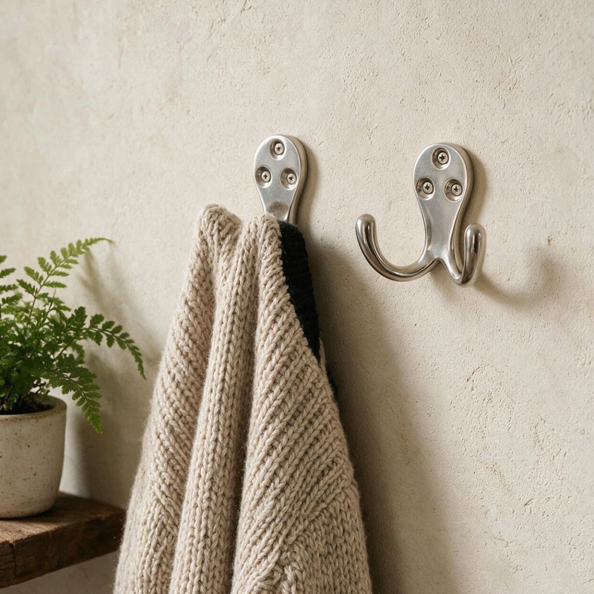 A Pair of Polished Nickel Double Pronged Coat Hook Mounted on a Wall with a Cardigna Hanging From One - Digital Illustration 