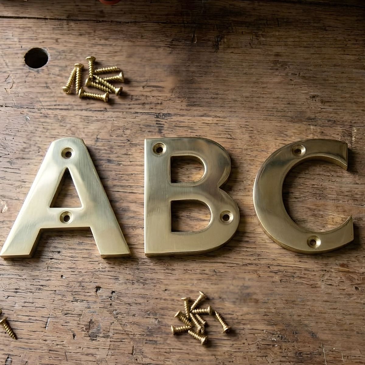 A Selection of Polished Brass 3 Inch Screw Fix Letters Laid out on a Wooden Work Bench - Digital Illustration