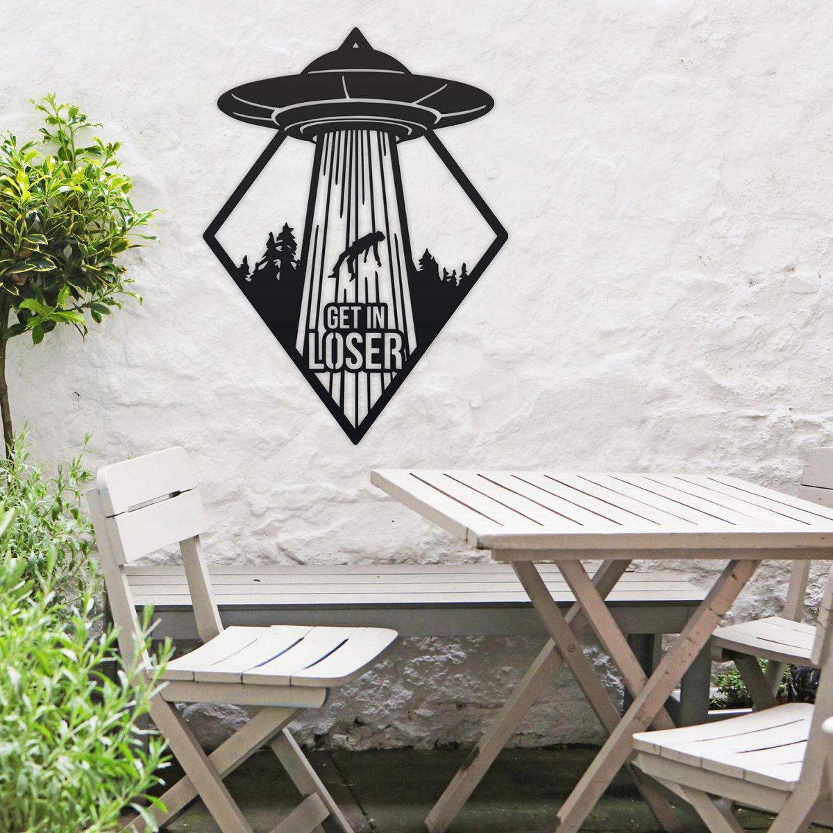 "Get in Loser" Alien Wall Art in Situ by a Wooden Table Set in the Garden