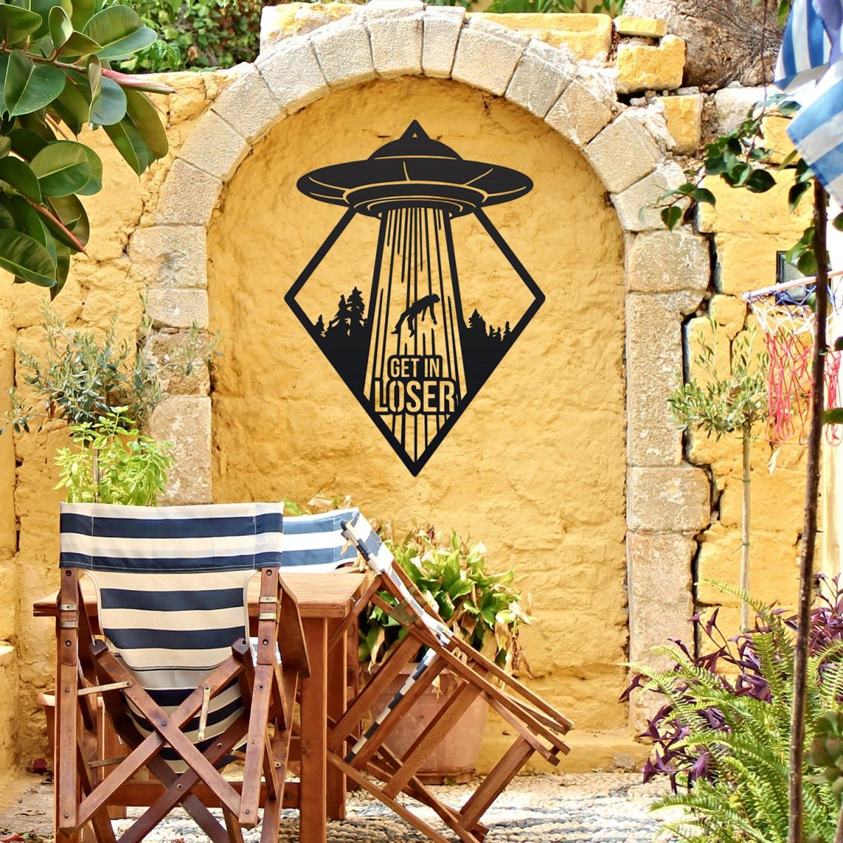 "Get in Loser" Alien Wall Art on a Yellow Brick Wall in the Garden